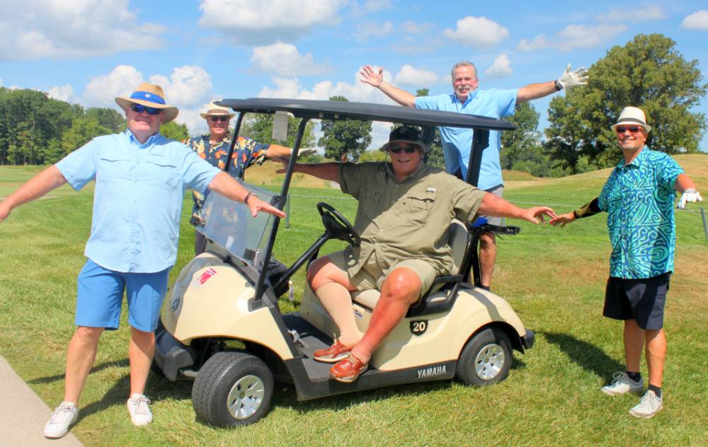 five alumni posing around a golf cart